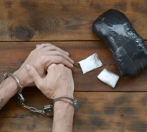 a man's hands in handcuffs next to drugs on a table