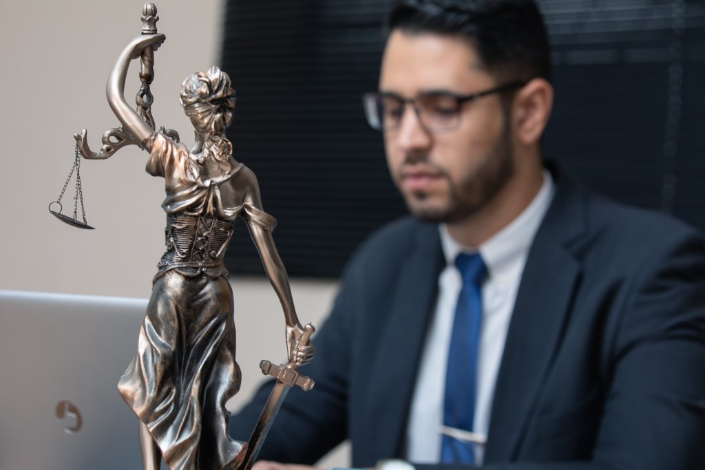 a lawyer in the background with a lady justice statue in the foreground