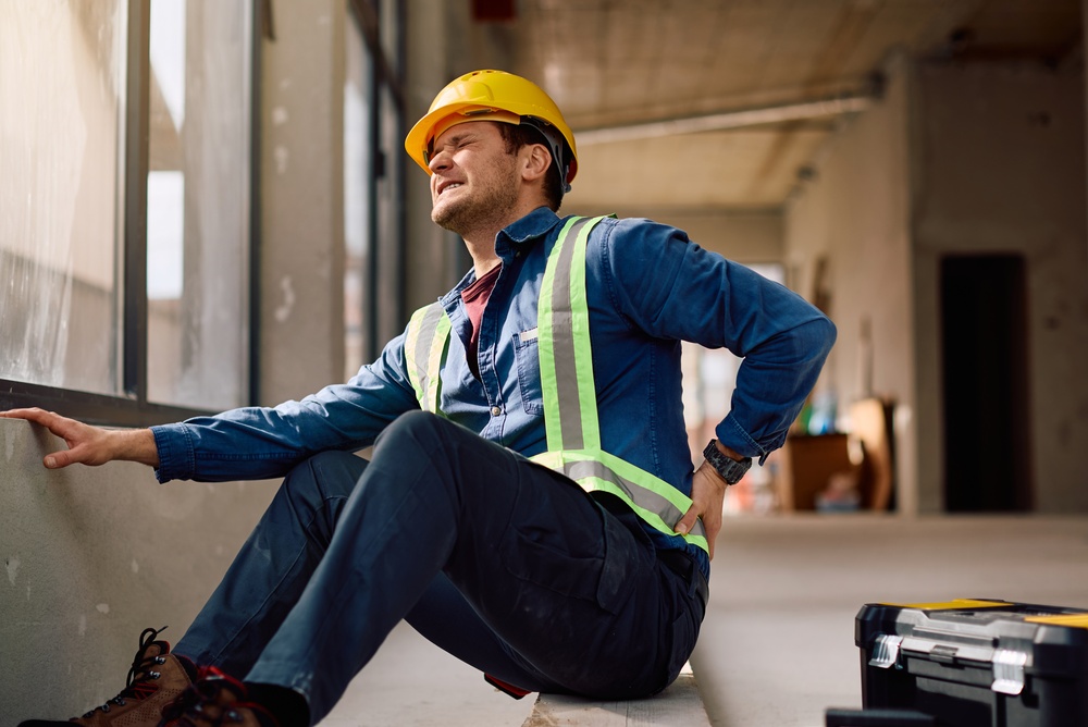 Construction worker holding his lower back in pain while working at building site. 