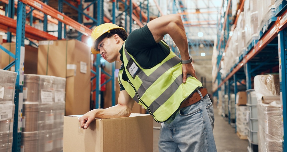 Logistics, loader and man with backache in warehouse, injury and stock distribution or supply chain. Shipping, joint pain and person with muscle tension, workplace accident and safety risk in factory